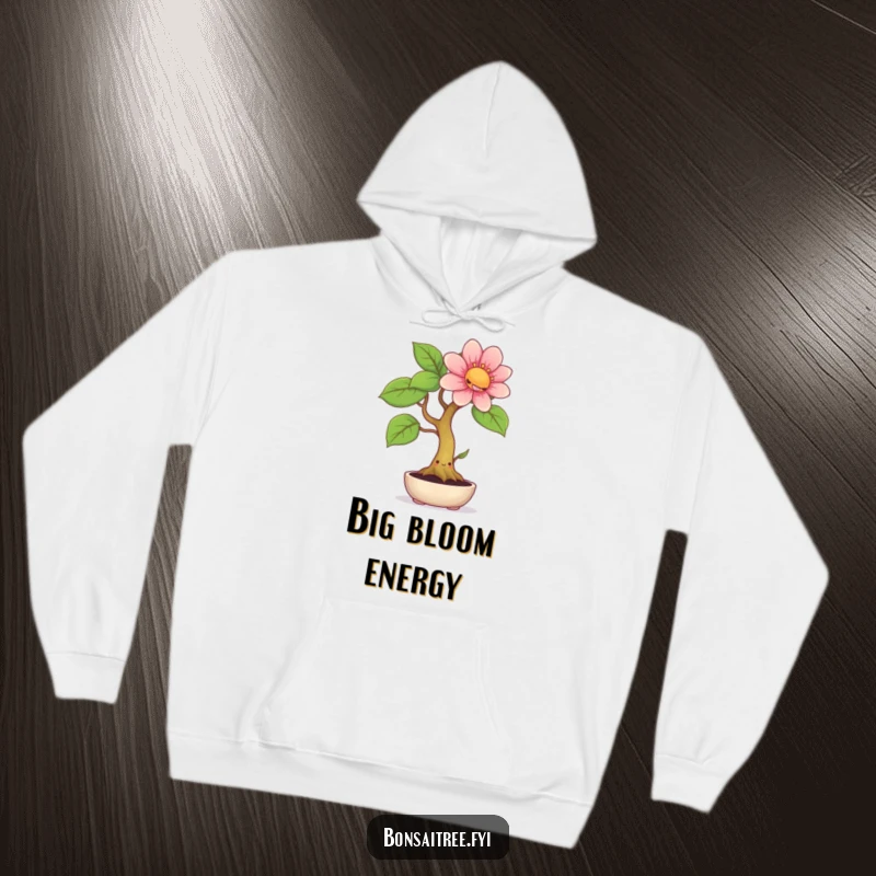 Funny hoodie depicting a smiling bonsai tree with a cheerful face, producing an unexpectedly large and beautiful flower, perfect for cozy laughs.
